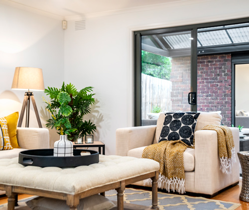 Cozy living room with stylish furniture including a light-colored armchair with decorative pillows a round coffee table and a floor lamp surrounded by greenery creating a relaxing atmosphere